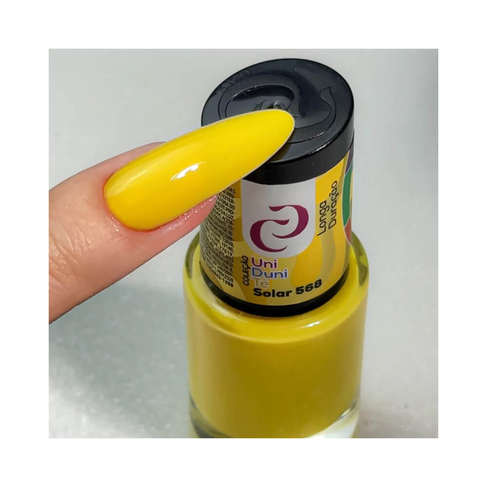 Unha com esmalte amarelo vibrante da coleção Uni Duni Tê da marca Cora, cor Solar 568, segurando o frasco do esmalte